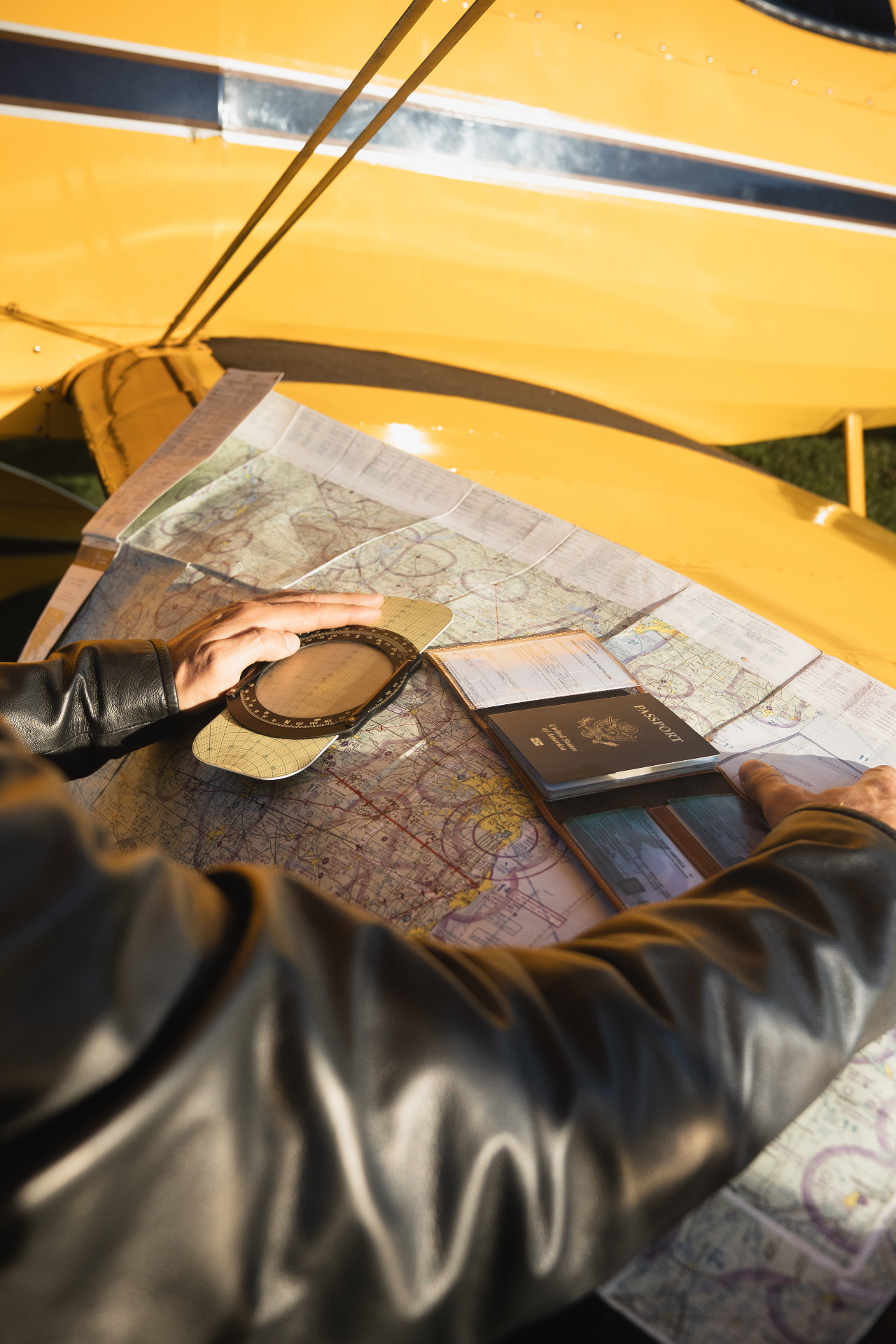 Pilot hands holding an open leather wallet with passport over an aviation sectional chart beside a yellow aircraft wing